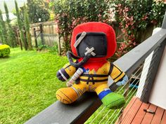 a stuffed toy sitting on top of a wooden fence next to a green lawn and bushes