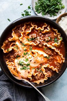 a skillet filled with lasagna shells and sauce on top of white rice