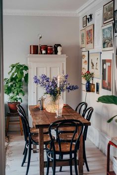 a dining room table with chairs and pictures on the wall above it, along with vases filled with flowers