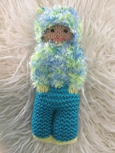 a crocheted doll wearing blue and green pants on a white furnishing