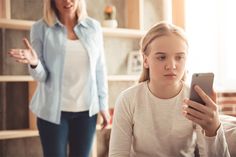 a woman looking at her cell phone while standing next to another woman in the living room