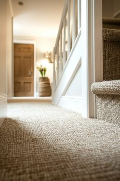 a carpeted hallway with stairs leading up to the first floor and another room in the background