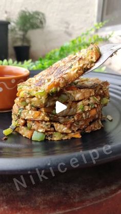 a stack of food sitting on top of a black plate next to a small bowl