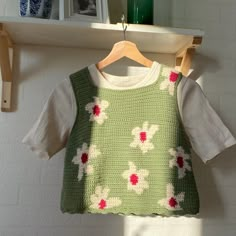 a green and white knitted sweater hanging on a wooden hanger next to a shelf