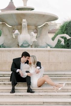 a man and woman are sitting on the steps in front of a fountain, kissing