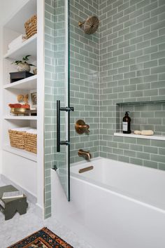 a white bath tub sitting next to a walk in shower under a bathroom window with green tiles on the walls