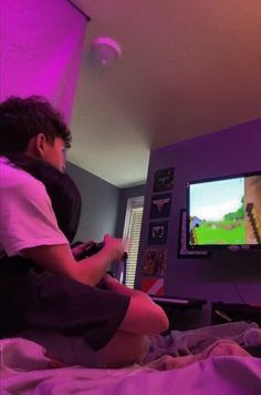 a young man sitting on top of a bed in front of a tv