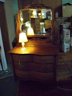 an old dresser with a mirror and lamp on it in a room filled with boxes