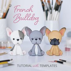 three little french bulldog figurines sitting next to each other on a table with paintbrushes