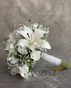 a bridal bouquet with white flowers and baby's breath on the side, sitting on a gray surface