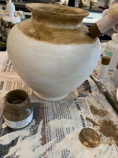 a large white vase sitting on top of a table next to paint and other items