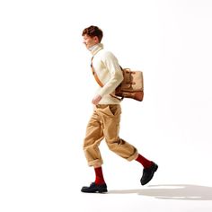 a man walking while carrying a bag and wearing brown pants, white sweater and red socks