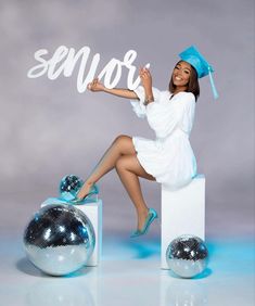 a woman in a graduation cap and gown sitting on top of a block with disco balls