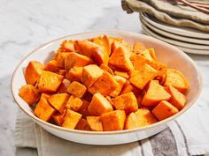 a white bowl filled with sweet potatoes on top of a table next to plates and utensils