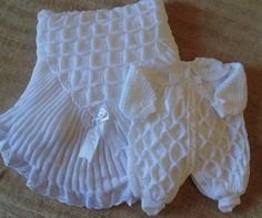 two white knitted baby clothes laying on top of a bed next to each other