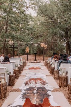 an outdoor ceremony with white chairs and brown cow hide rugs on the ground, surrounded by trees