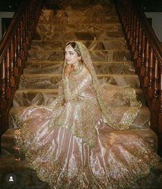 a woman sitting on top of a set of stairs wearing a gold dress and veil