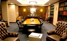 a large conference room with leather chairs and a wooden table in the center surrounded by bookshelves