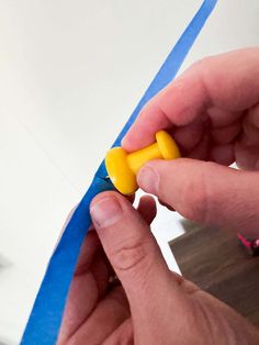 someone is cutting out the end of a piece of blue tape with yellow plastic scissors