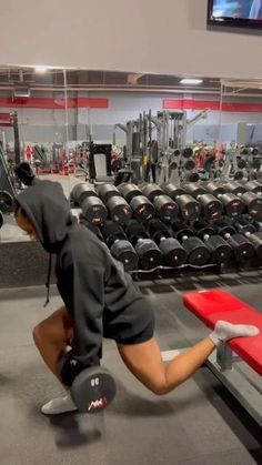 a man squatting down in front of a row of dumbbells at a gym