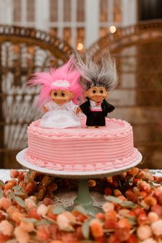 two dolls are sitting on top of a pink cake