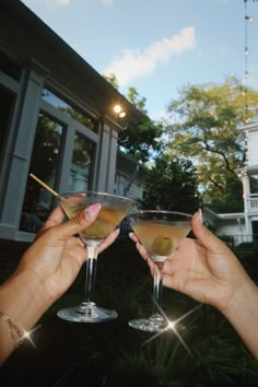 two people holding up martini glasses in front of a house