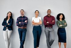 four people standing in front of a gray wall with their arms crossed and looking at the camera