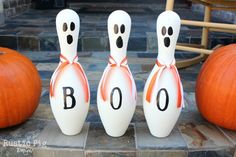 three white bowling pins with the word boo painted on them sitting next to pumpkins