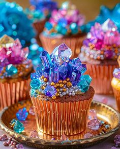 cupcakes decorated with colorful crystals and beads on a gold plate, surrounded by other muffins