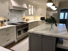 a kitchen with white cabinets and marble counter tops, along with an island in the middle