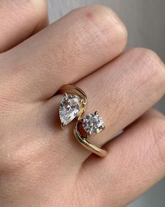 a woman's hand wearing a gold ring with two pear shaped diamonds