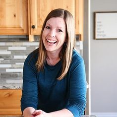 a woman sitting at a kitchen counter smiling for the camera with her hands folded out