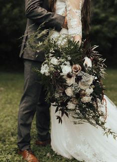 a bride and groom standing in the grass with their arms around each other holding a bouquet