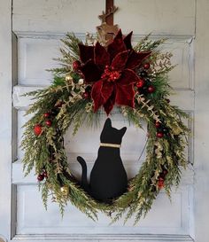 a black cat sitting in front of a christmas wreath on a white door with poinsettis