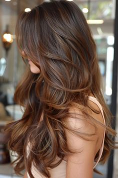 Woman with long, wavy brown hair in a modern salon. Light Brown Hair With Red Highlights Caramel, Barely Red Hair, Chocolate Hair Caramel Highlights, Brown Hair Caramel Lowlights, Brown Reddish Hair With Highlights, Caramel Brown Hair Color Honey, Cinnamon Brunette Balayage, Soft Cinnamon Hair Color, Brunette With Caramel Highlights Honey Hair Color Ideas