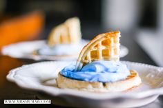 two waffles with blue icing are on a white plate next to each other