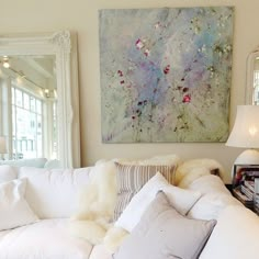 a living room filled with white furniture and pillows on top of a table next to a mirror