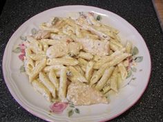 a white plate topped with pasta covered in sauce and chicken breast fillets on top of a black counter