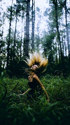 a woman laying in the grass with her hair blowing in the wind and trees behind her