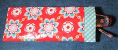 a red and blue flowered pouch with two zippers on the side, sitting on a blue surface