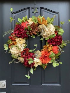 a wreath on the front door with flowers and leaves hanging from it's sides