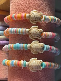 several bracelets with different colored beads and turtle head charms on them, hanging from a pink towel