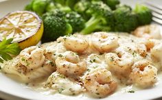 a white plate topped with shrimp and broccoli next to a slice of orange