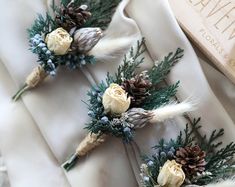 three boutonnieres with pine cones and white roses on them are sitting next to a book