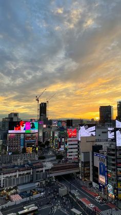 an aerial view of a city with tall buildings and billboards in the background at sunset