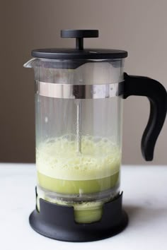 a blender filled with green liquid on top of a white counter next to a black handle