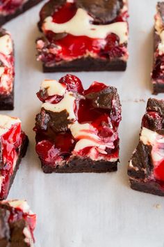 several pieces of brownie with cherries and white chocolate on top, sitting on a baking sheet