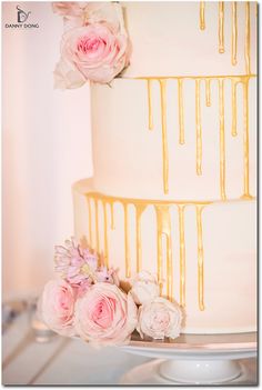 a three tiered cake with flowers and dripping icing on the top, sitting on a table