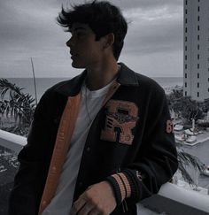 a young man standing on top of a balcony next to the ocean with his hands in his pockets