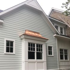 a gray house with a copper roof and white trim on the front door is shown